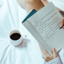 crop woman with coffee writing in notebook on bed